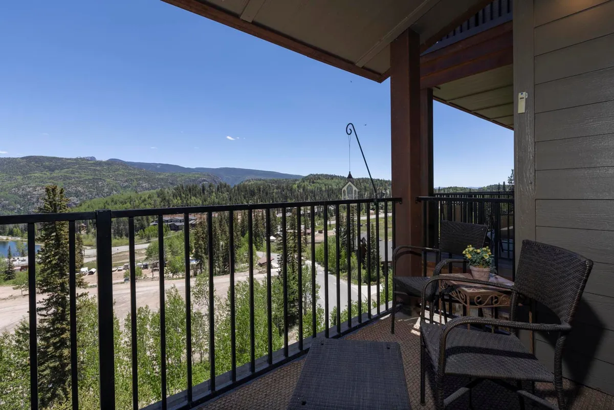 The hero image showcases a serene mountain view from the balcony of the condo, with comfortable outdoor furniture inviting guests to relax. Lush green trees fill the foreground, while the majestic Needles Mountains rise in the background, bathed in soft natural light. The scene evokes tranquility and connection with nature, perfect for unwinding or enjoying morning coffee.