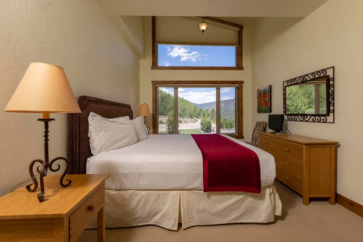 A serene bedroom featuring a cozy queen-sized bed, large picture windows, and a decorative mirror. The windows open to stunning views, blending indoor comfort with the natural beauty just beyond.