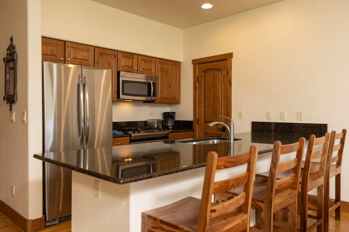 A beautifully designed kitchen featuring a granite countertop, wooden bar stools, stainless steel appliances, and warm wooden cabinetry. The open layout invites socializing and makes meal preparation a communal, enjoyable experience.