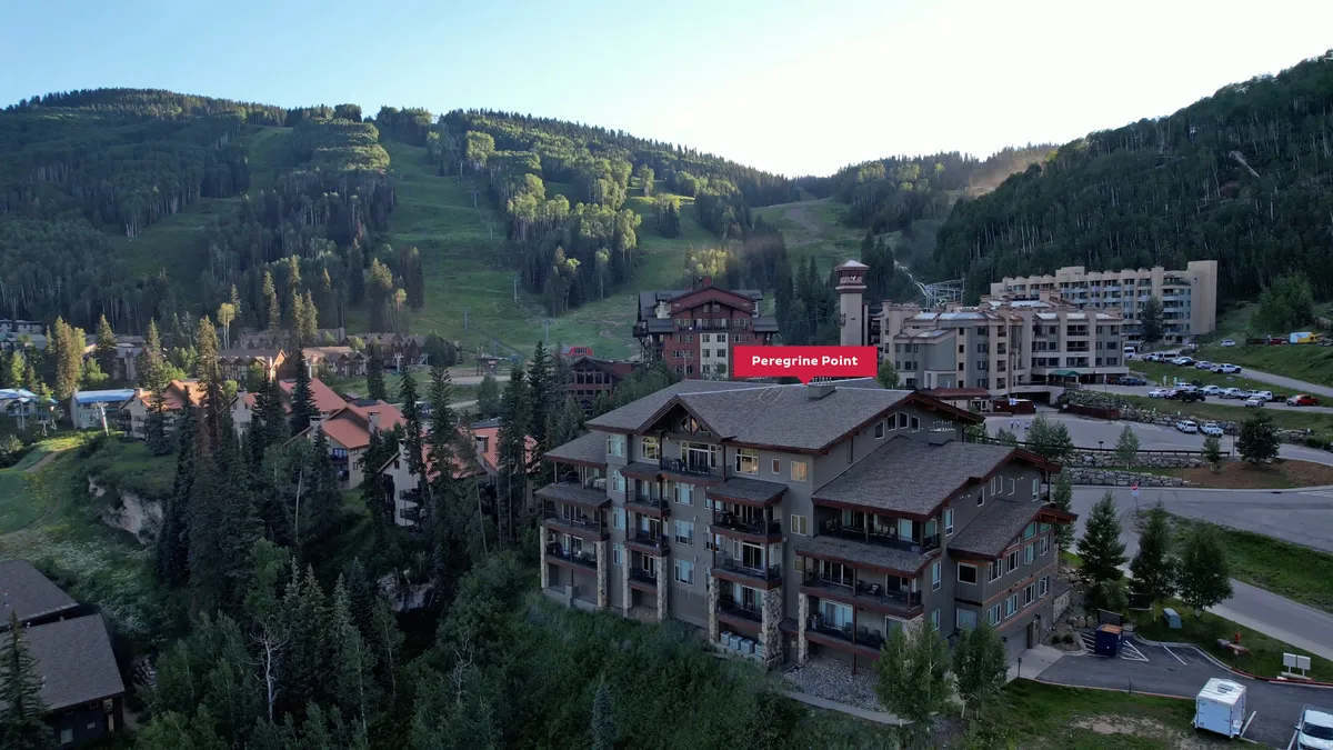 The exterior of Peregrine Point stands amidst lush green forests, with the majestic Needles Mountains as a backdrop. The building’s balconies overlook the natural surroundings, and the peaceful setting is ideal for stepping out onto the trail network. The parking area suggests easy access for day trips and exploration.