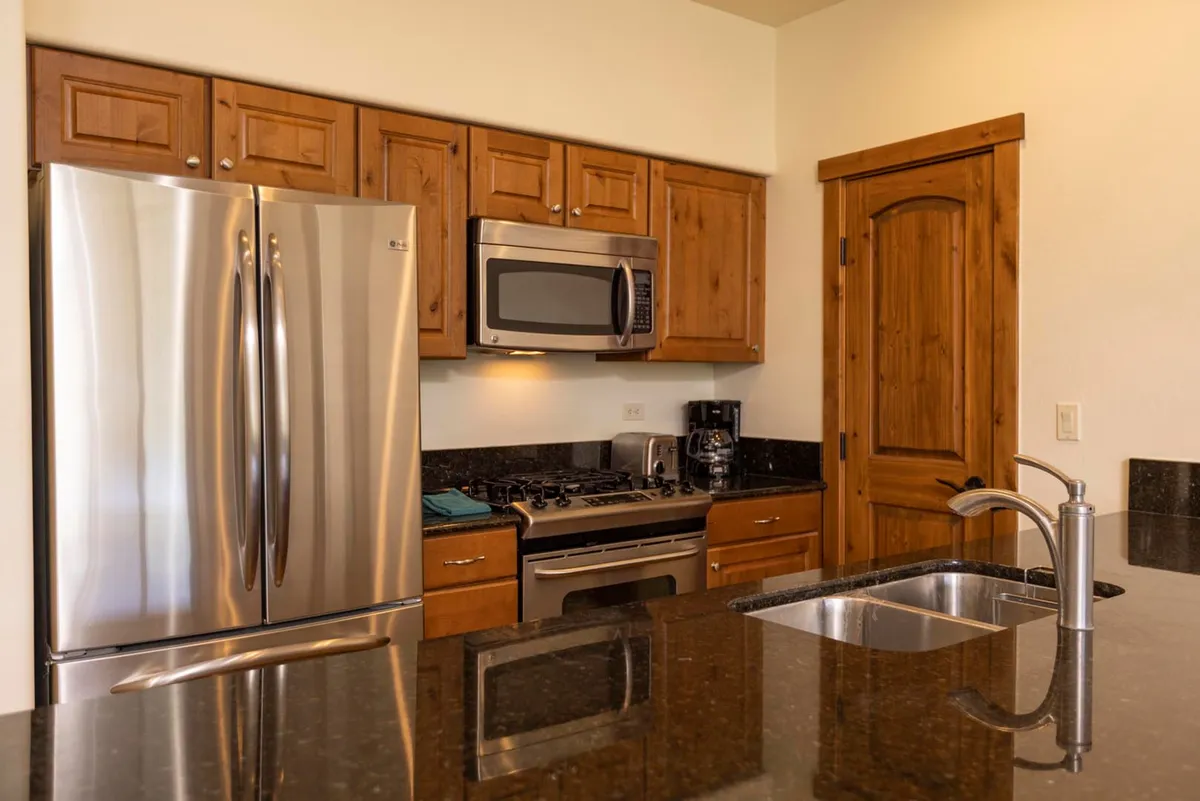 A modern, fully equipped gourmet kitchen featuring stainless steel appliances, granite countertops, and wooden cabinetry. The spacious layout encourages group cooking sessions, meal prep, and family traditions.