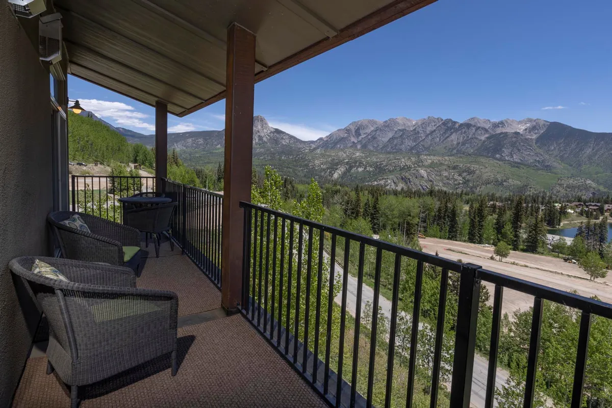A private balcony with outdoor seating overlooks a stunning expanse of snow-dusted mountains. The balcony rail frames the dramatic mountain vistas, while the peaceful ambiance suggests the perfect spot for sunset alpenglow or morning coffee. The setting invites relaxation and reflection, connecting the interior comfort to the majesty outside.